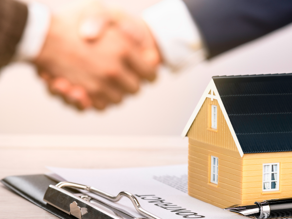 Two business men shaking hands near documents and a model small house