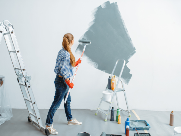 Woman with roller paints the wall grey-blue