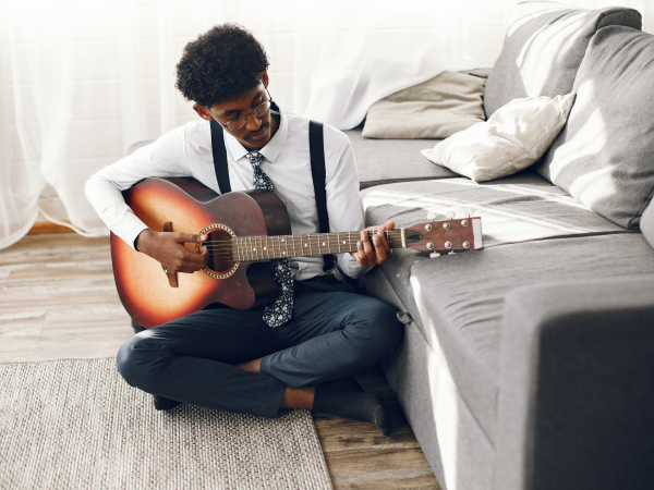 Young indian man playing guitar in living room with soundproof curtains