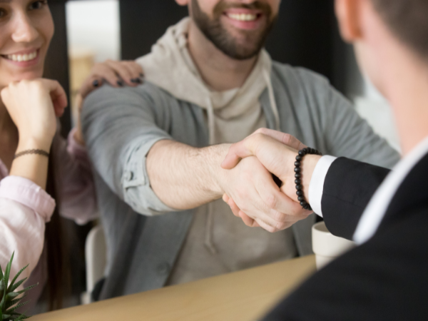 eal estate agent shaking hands with happy couple