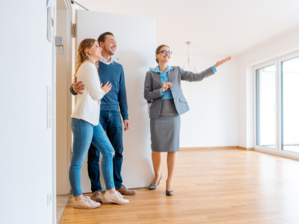 female real estate agent showing open plan house to young couple