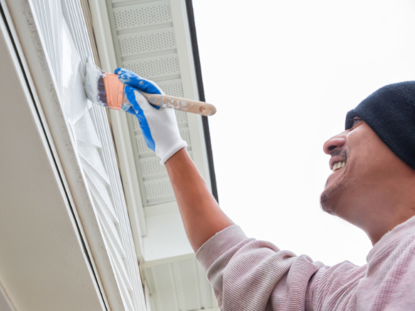 man holding a paintbrush and happily painting his homes exterior