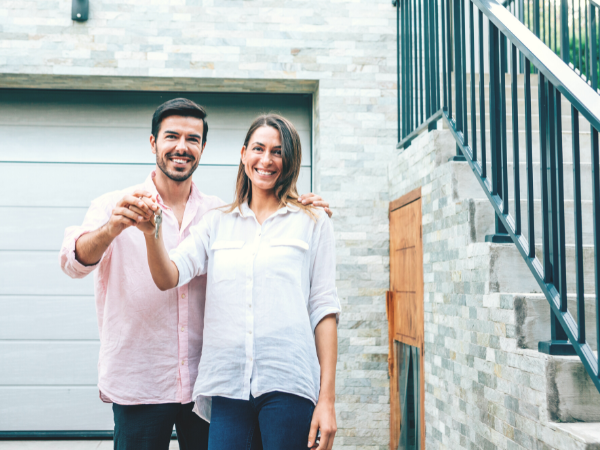 happy first-time buyers holding key and standing in front of new home's garage door