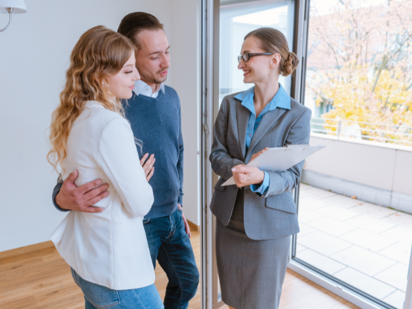 young couple discussing lease agreement with smiling property practitioner