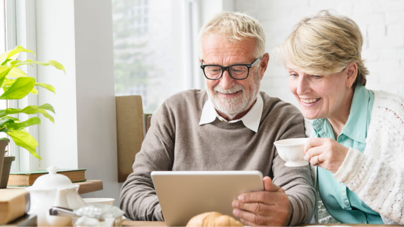 happy retired couple smiling and looking at tablet
